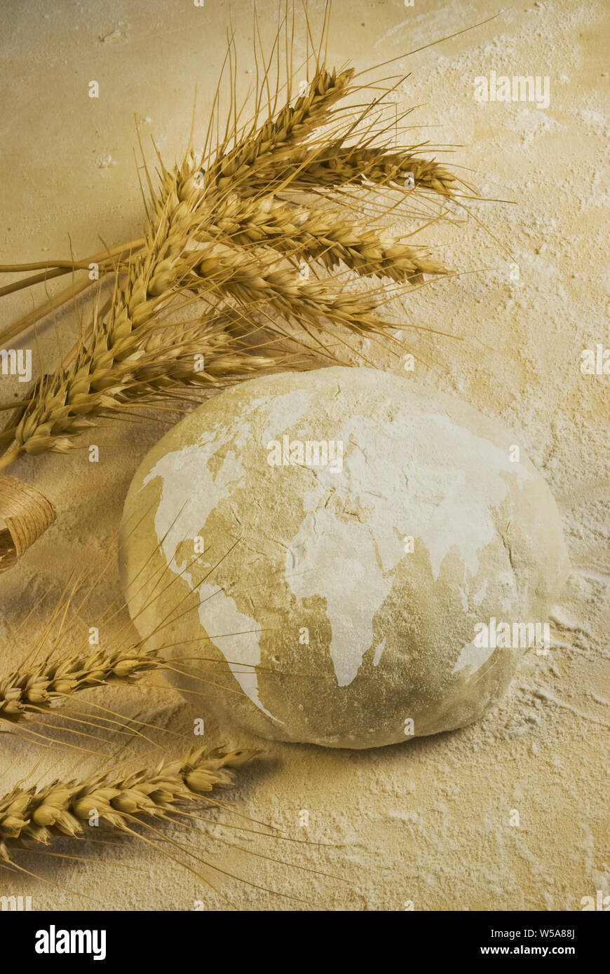 conceptual.Flour dough and water form a ball on which a map of the world is drawn and some ears of wheat on the table Stock Photo