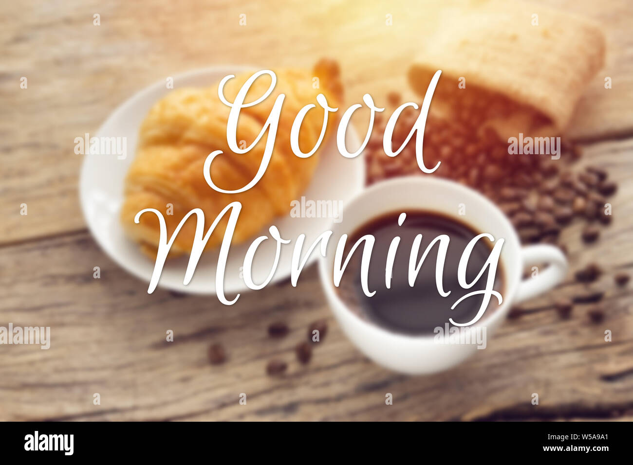 text good morning with blurry of continental breakfast with fresh croissant and hot coffee on wooden table, decoration with coffee bean as background Stock Photo