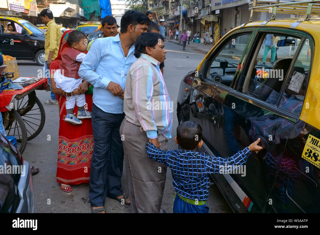 Members of a large Indian family trying to persuade a taxi driver to transport them, despite the four passenger maximum limit; Mumbai, India Stock Photo