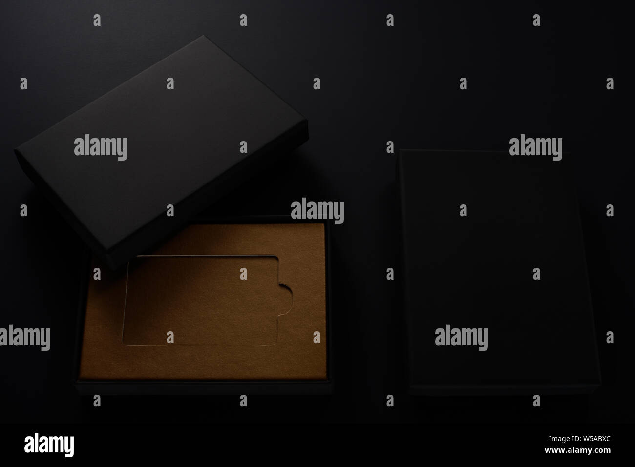 Slick black gift boxes with brown cardboard inside on black background Stock Photo