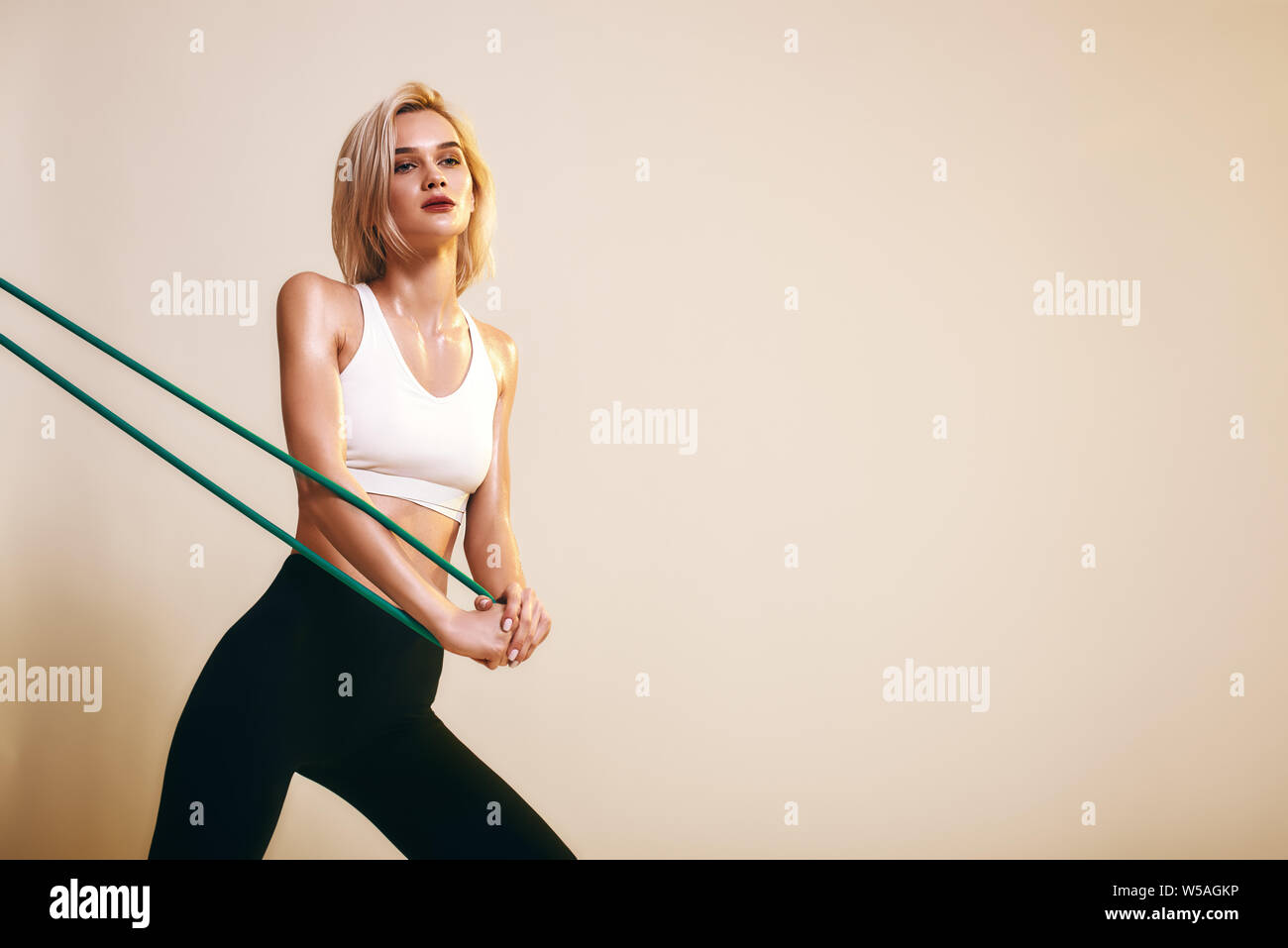 Flexibility. Sporty young woman in white top and black leggings working out with elastic band while standing in studio. Sport concept. Sport equipment Stock Photo