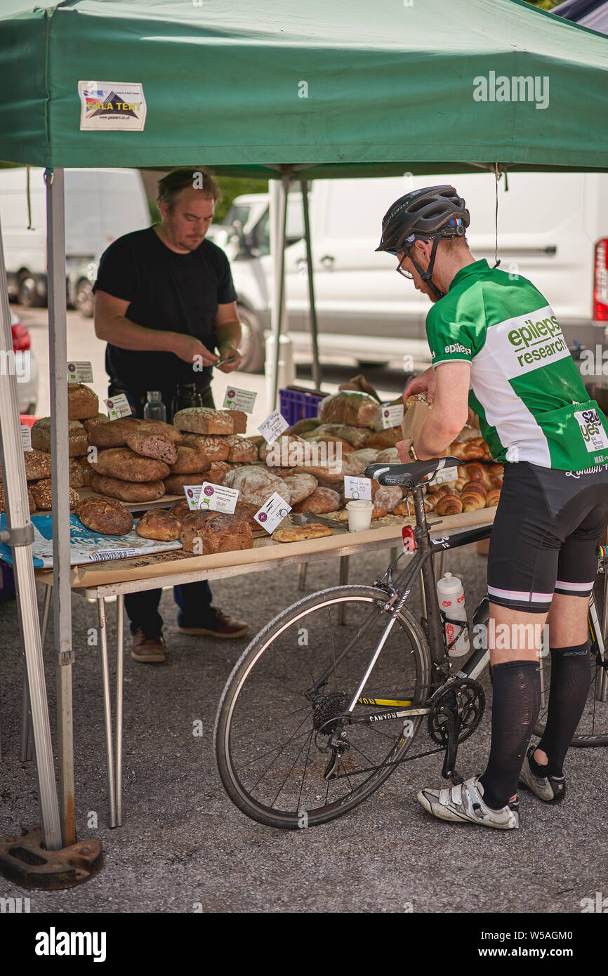 London, UK - July, 2019. A cyclist buying bread in an organic bakery stall in Brockley market, a local farmer's market held every Saturday in Lewisham. Stock Photo