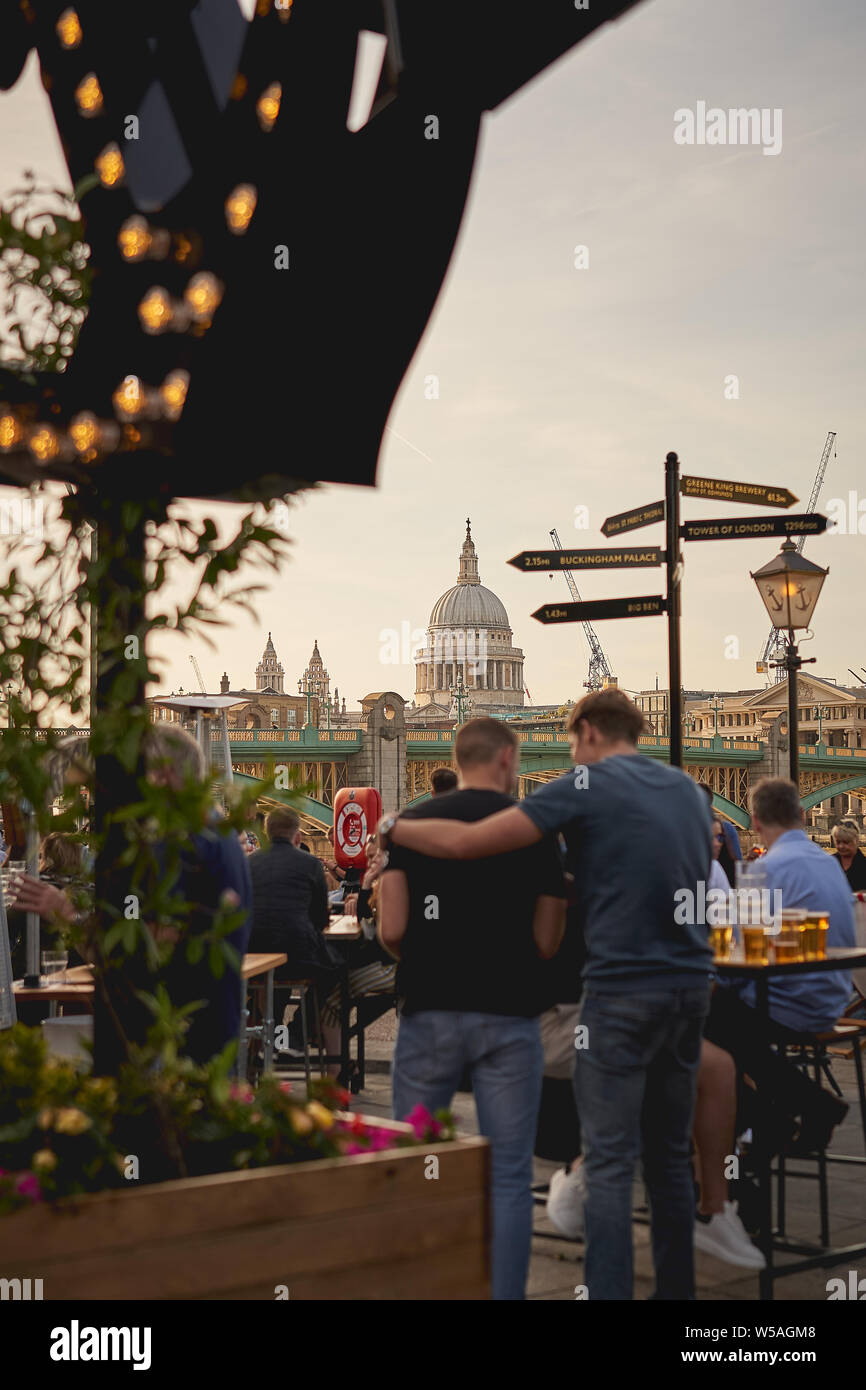 London, UK - July, 2019. Young people having drinks in a pub on a Friday night after work, with St. Paul's Cathedral on the background. Stock Photo
