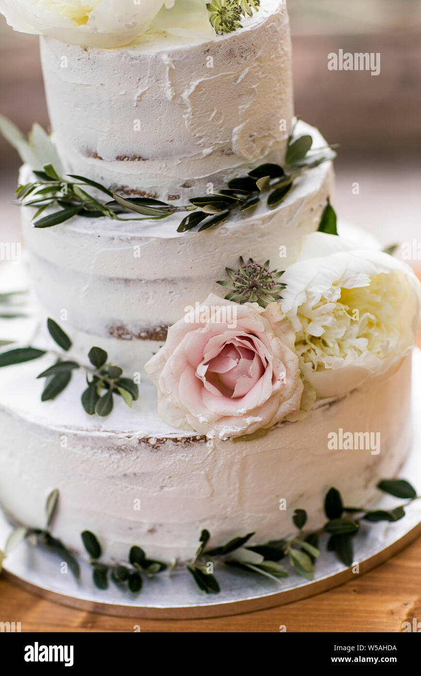 Naked wedding cake in boho chic style decorated with olive branches, pink roses and white peonies. Portrait format. Stock Photo