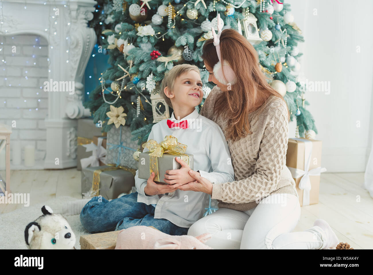 Mom and son under Christmas tree. Smiling mother giving Christmas gift ...