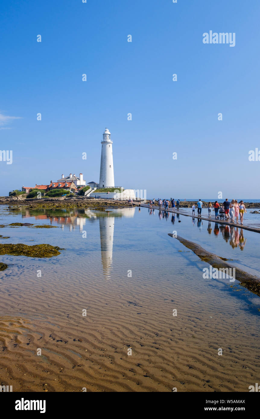 On Northumberland coast - day trippers tourists and families walk across the causeway to St Mary's Lighthouse  at Whitley Bay North Tyneside Stock Photo