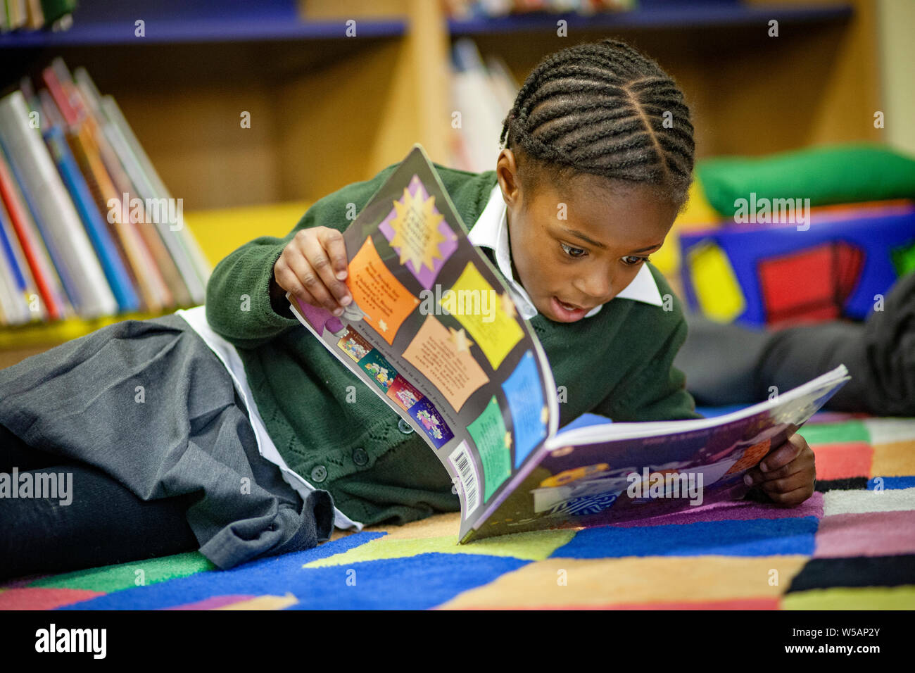 An Afro-Caribbean girl reading in a primary school library in the UK Stock Photo