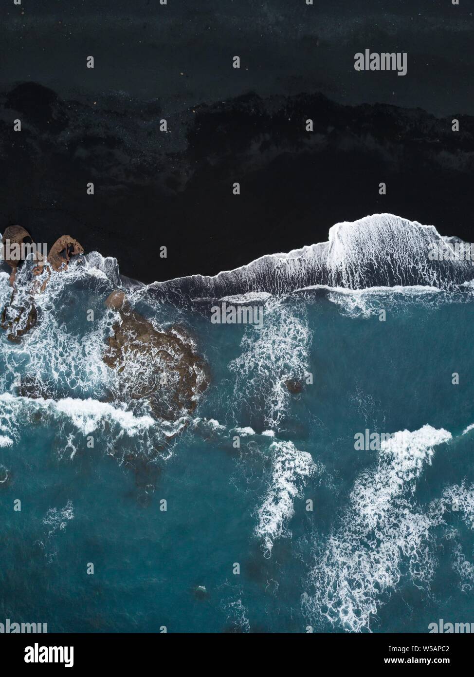 Black volcanic beach with rocks and waves running out from above, black ...