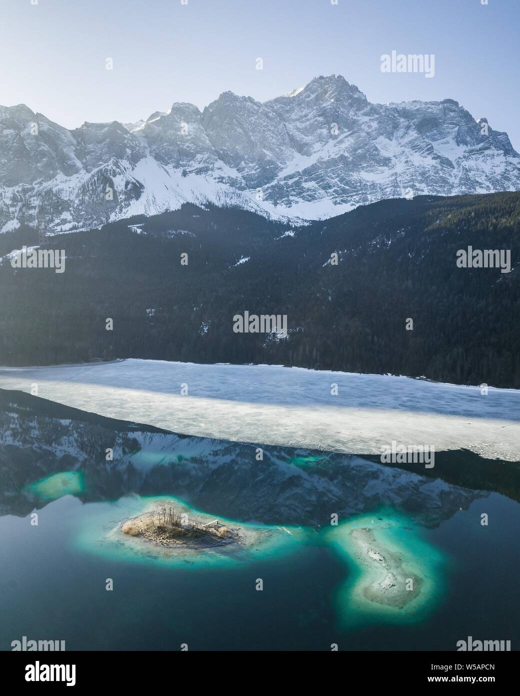 Eibsee lake, partly frozen in front of snow-covered mountains, change of season, Wetterstein range, drone shot, Garmisch-Partenkirchen, Germany Stock Photo