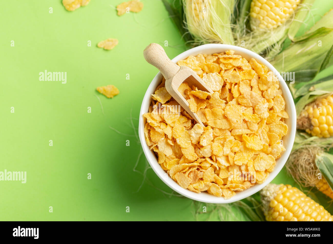 Corn flakes and corn cobs over green background, healthy food concept presentation Stock Photo
