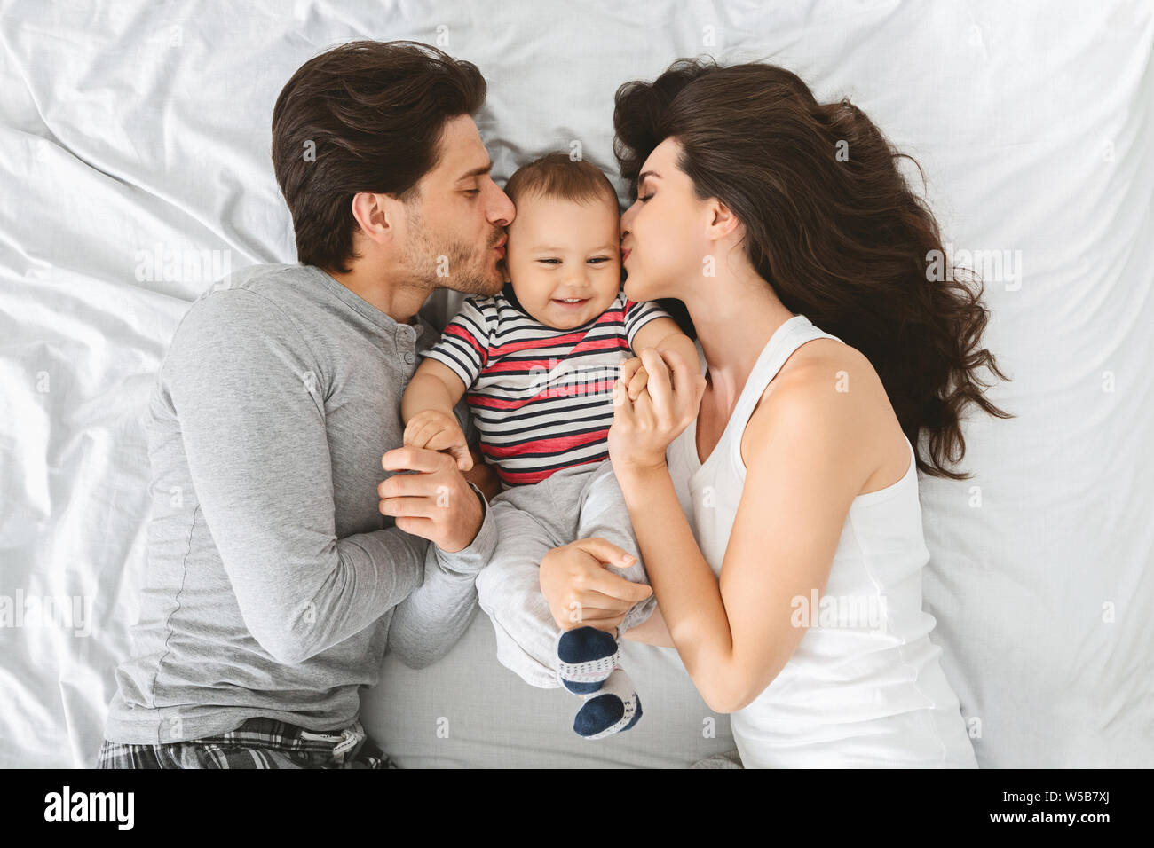 Happy caucasian couple kissing sweet cheeks of their adorable baby son Stock Photo