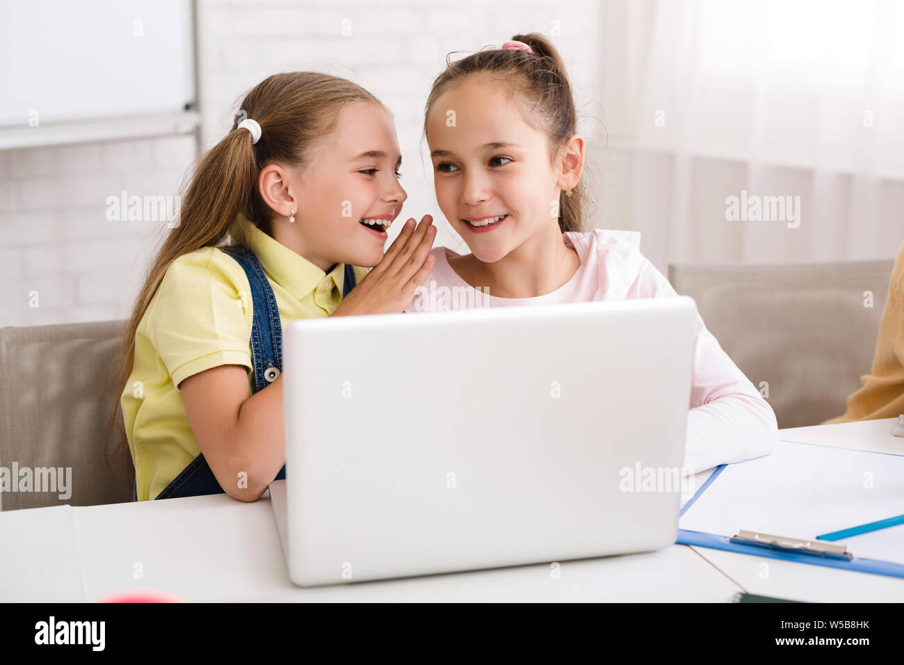 Classmates whispering and using laptop after lesson Stock Photo
