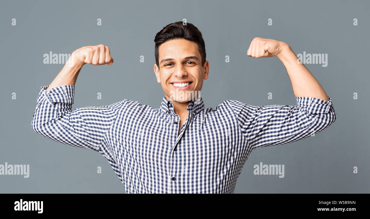 Positive young man showing biceps and smiling at camera Stock Photo