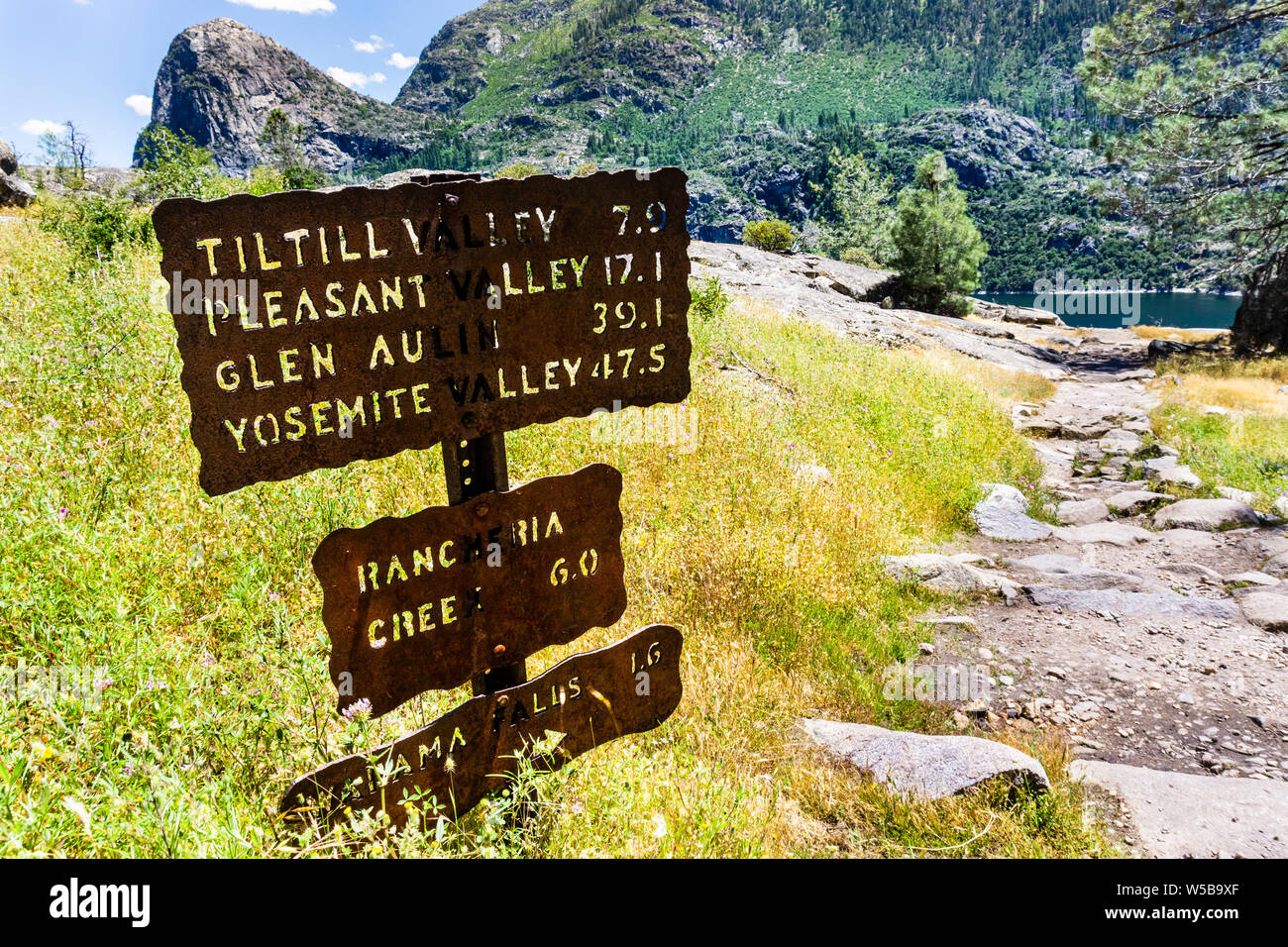 Hiking trail sign posted on the Wapama Falls trail, on the shoreline of Hetch Hetchy reservoir, showing points of interest and distances; Yosemite Nat Stock Photo