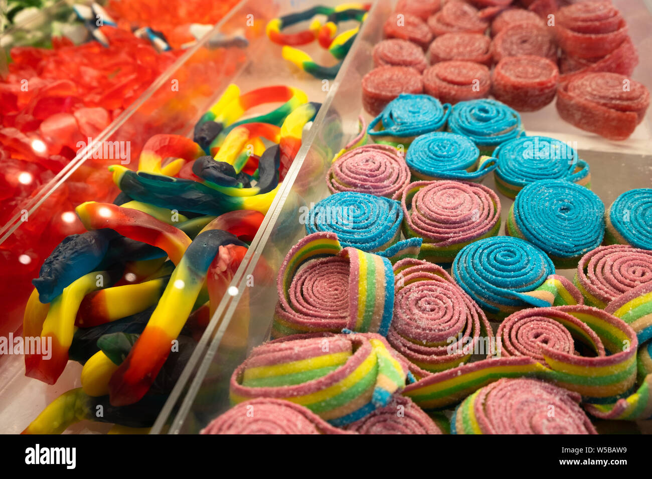 Colorful assortment of gummy candies and sour belts displayed in clear plastic bins at a candy store or market setting Stock Photo