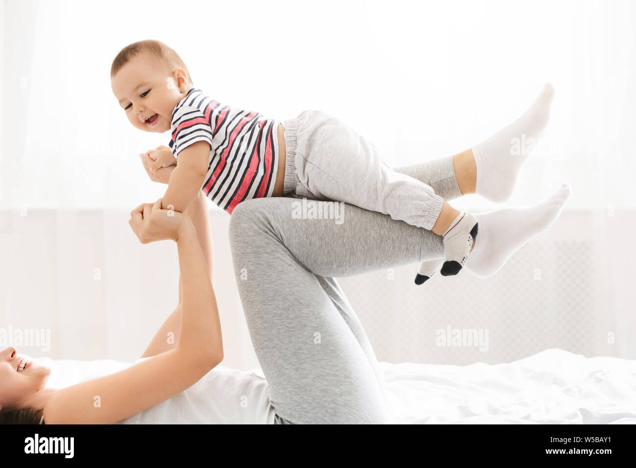 Millennial mommy playing with her baby son, lifting him up on legs Stock Photo