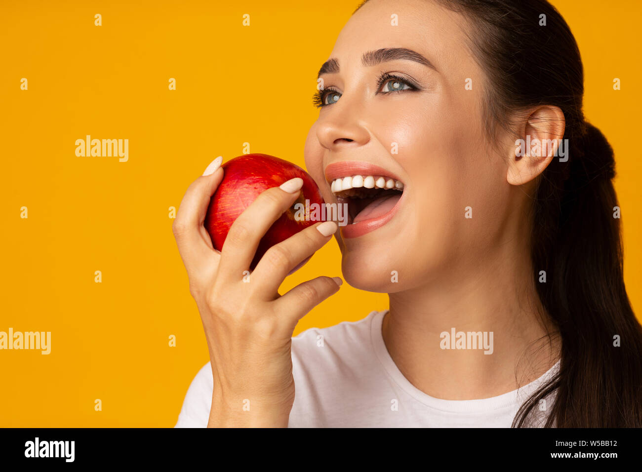 Girl With Perfect White Smile Holding Apple On Yellow Background Stock Photo