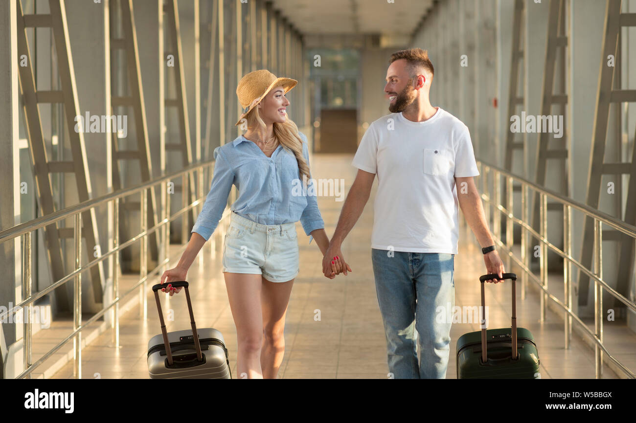 Happy couple going in airport terminal with luggage Stock Photo - Alamy