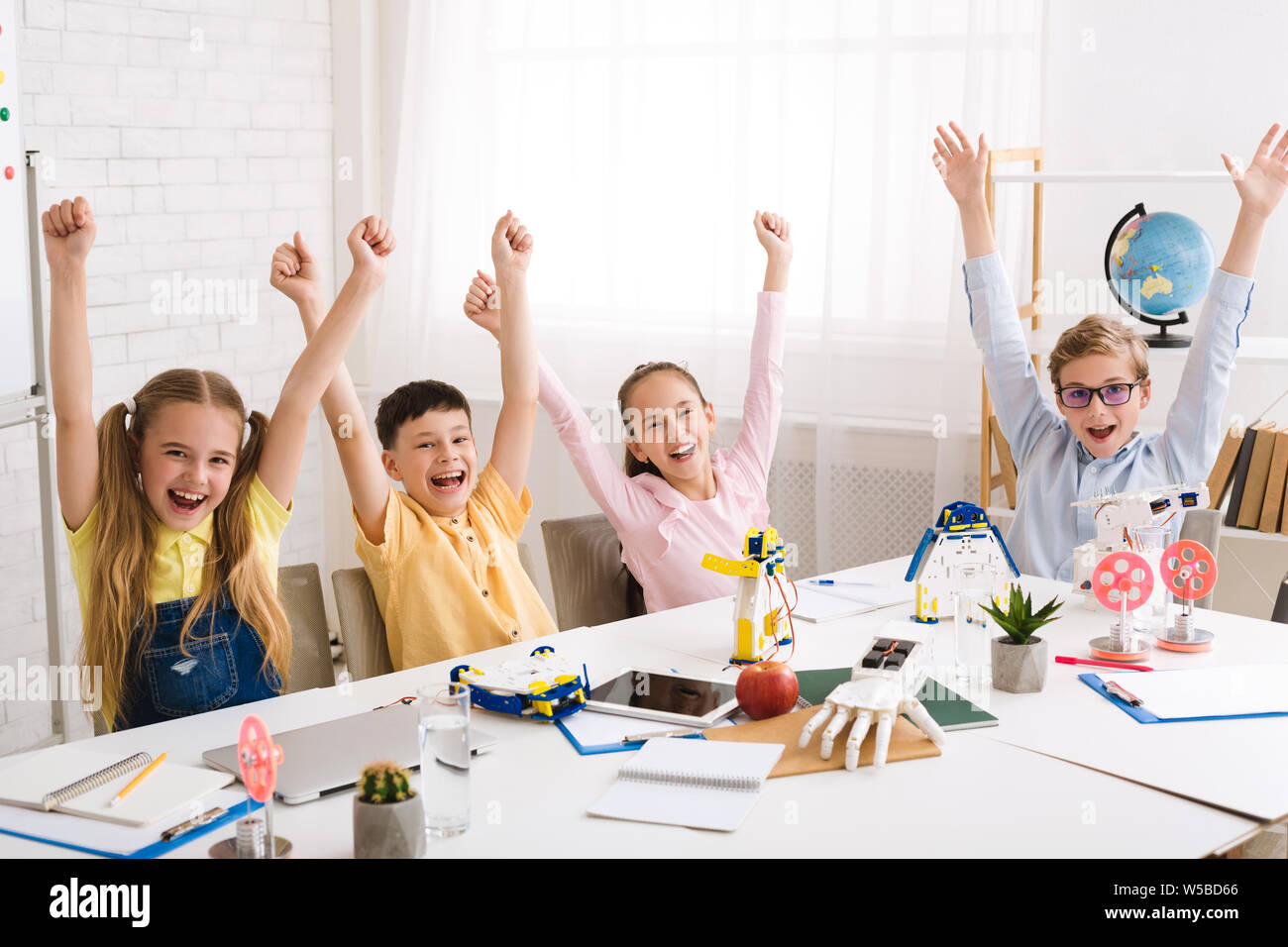 Happy classmates rejoicing with raised hands after STEM class Stock Photo