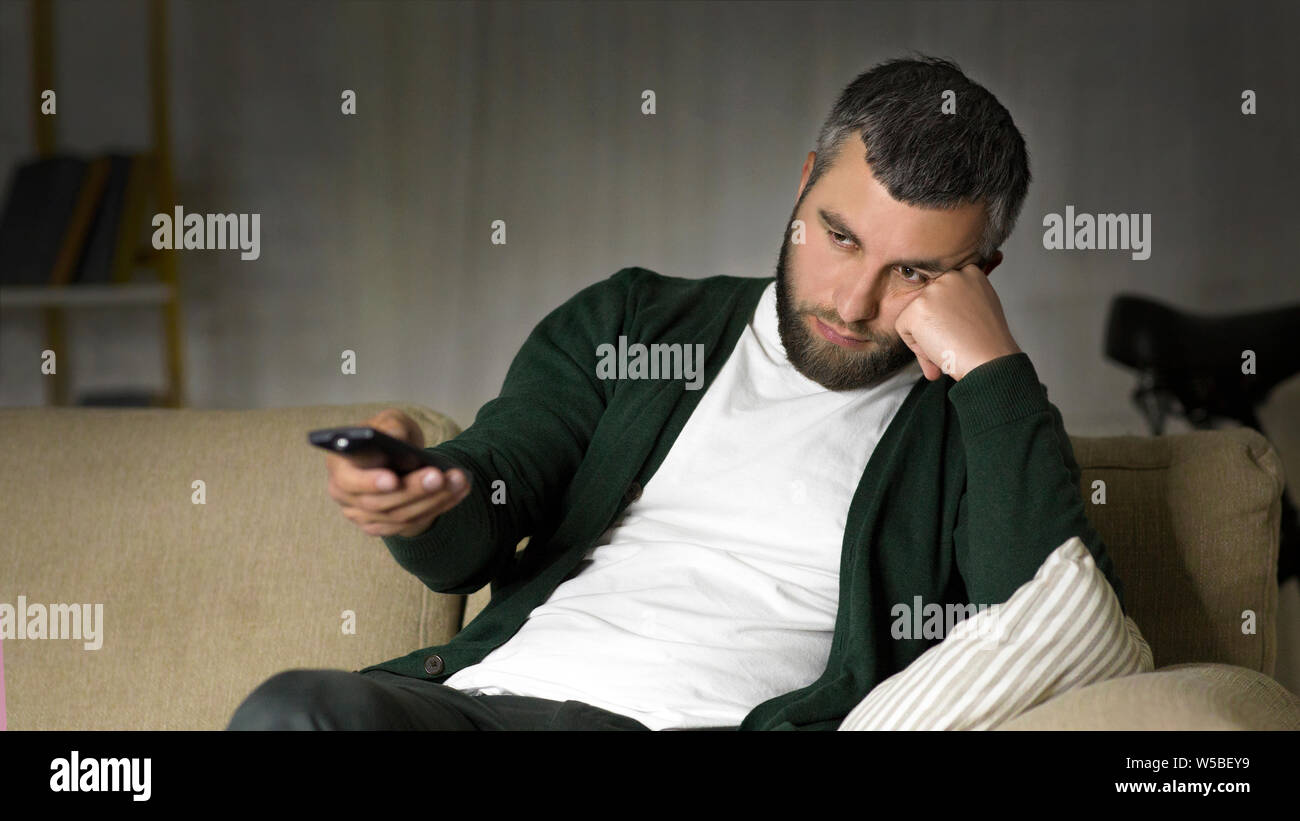 Bored man switching channels on TV at home Stock Photo