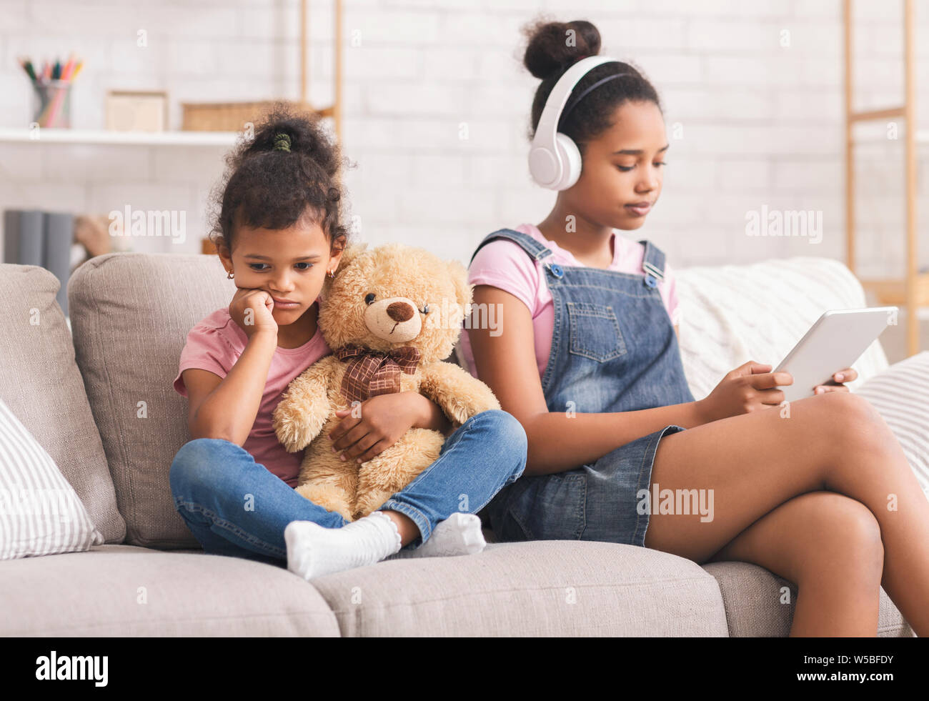 Little african girl boring alone, her elder sister watching videos Stock Photo