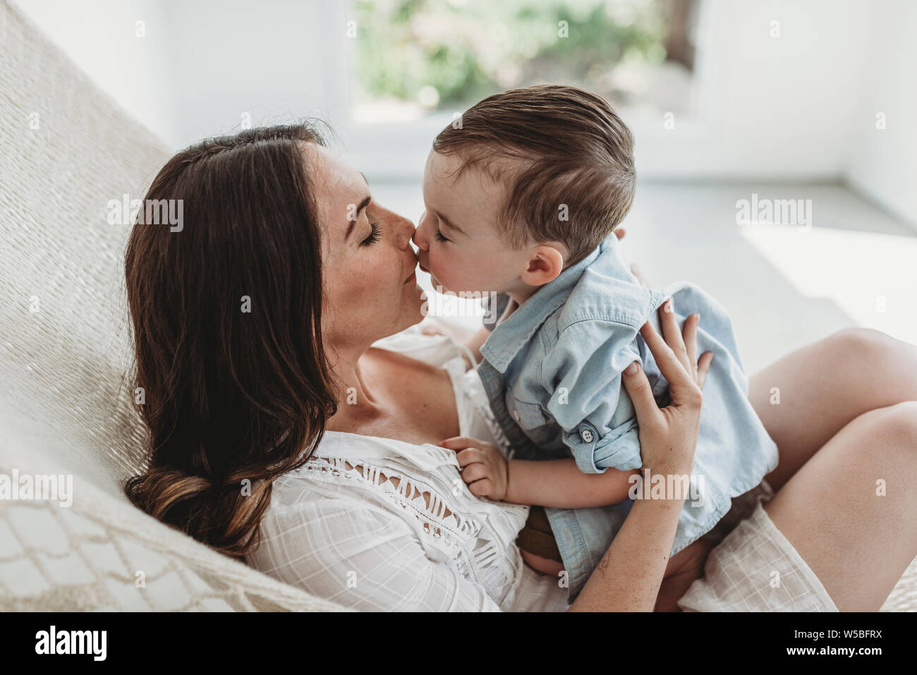Mother and Son kissing and cuddling in hammock in natural light studio Stock Photo