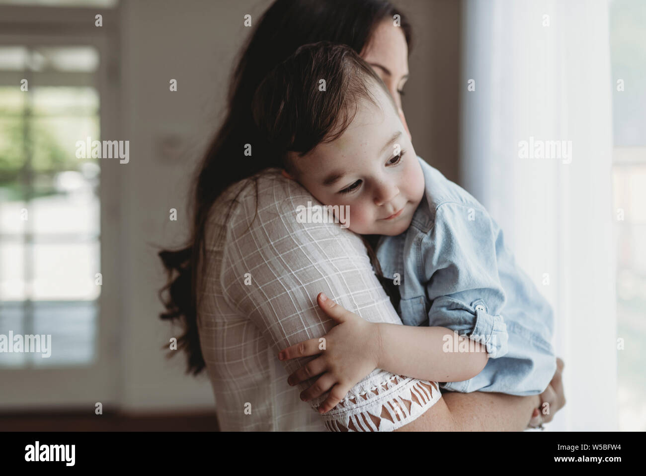 Close up of mother cuddling with young son in natural light studio Stock Photo