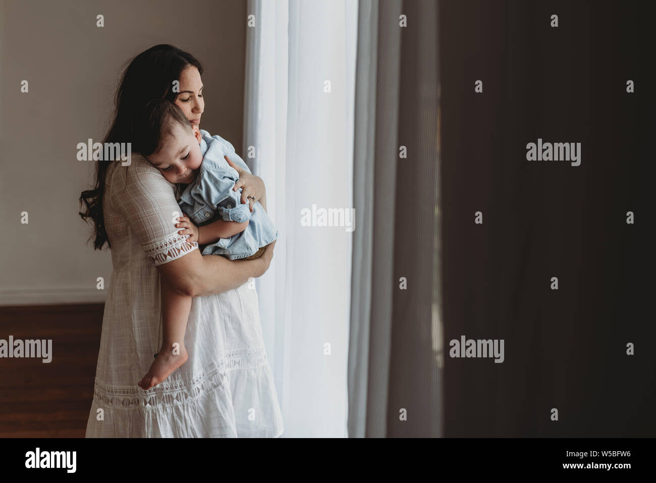 Young pregnant mother cuddling with young son in natural light studio Stock Photo