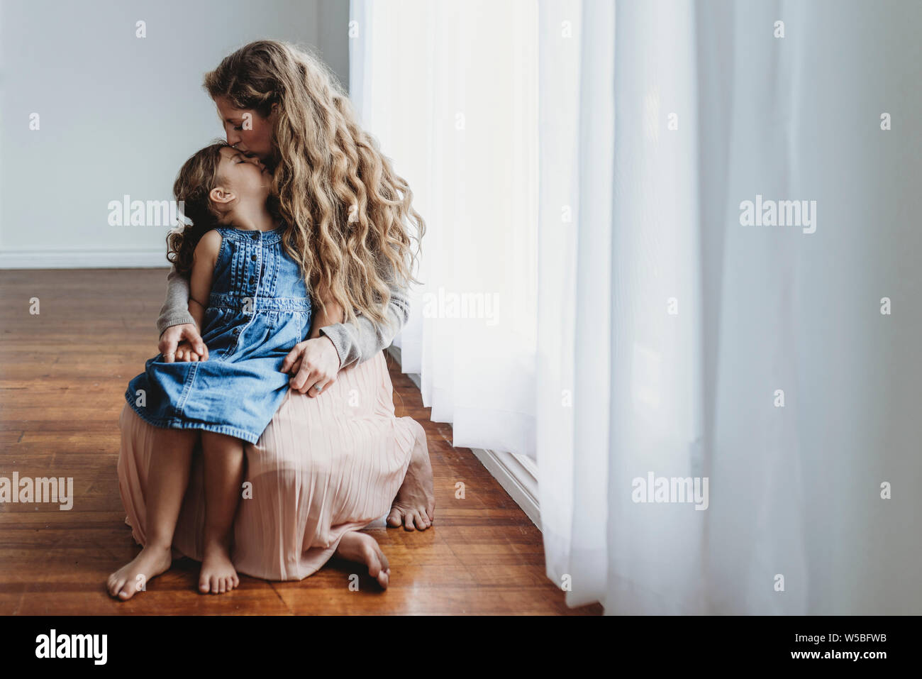 Full view of mother kissing daughter on forehead while holding hands Stock Photo