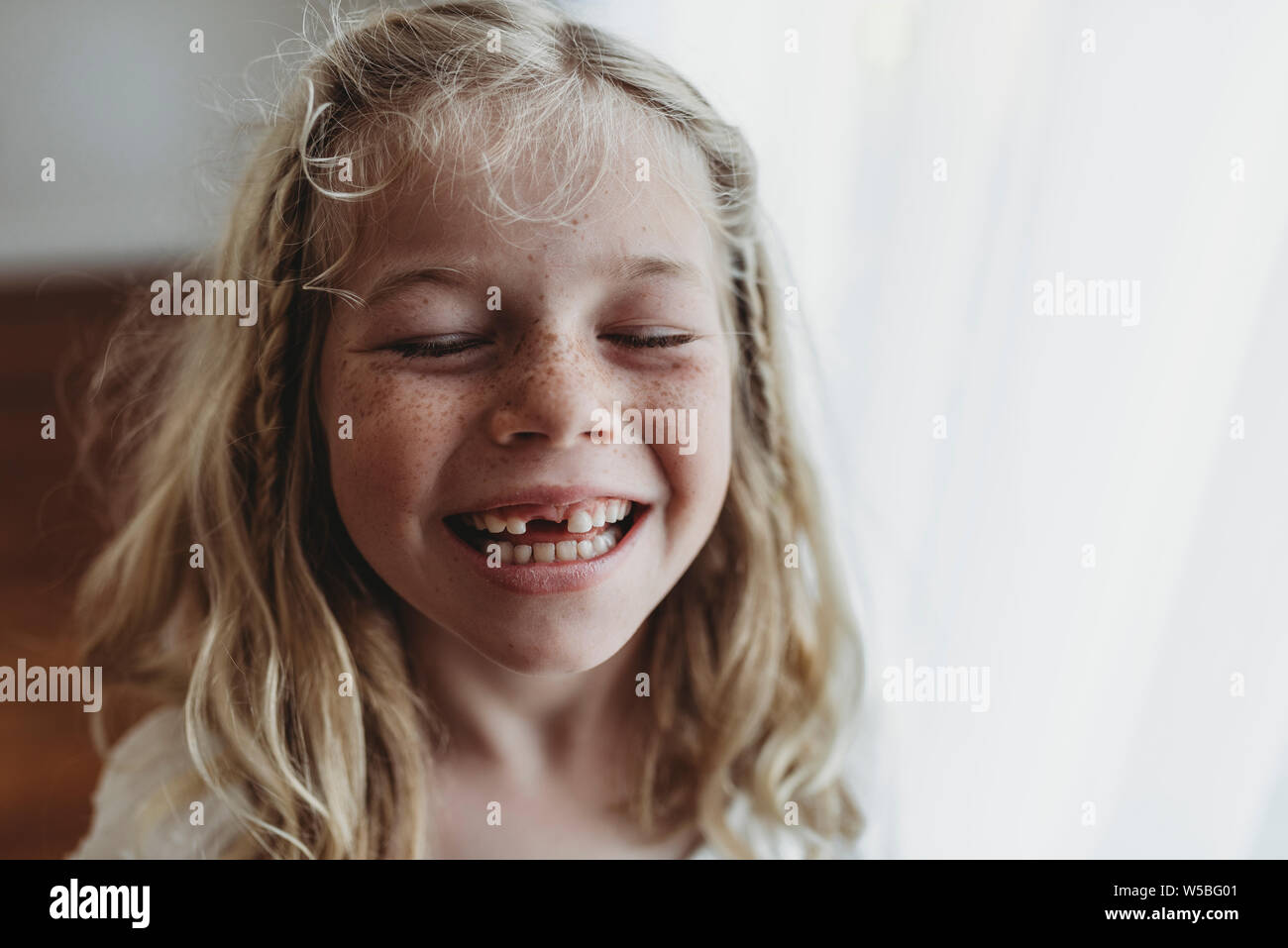 Portrait of young freckled smiling girl missing tooth with eyes closed Stock Photo