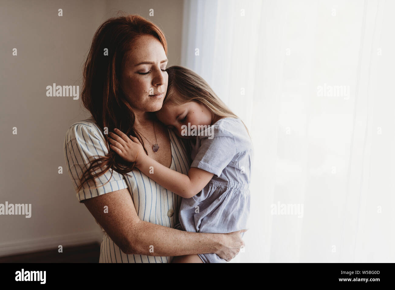 Young mother cuddling with young daughter while closing eyes in studio Stock Photo