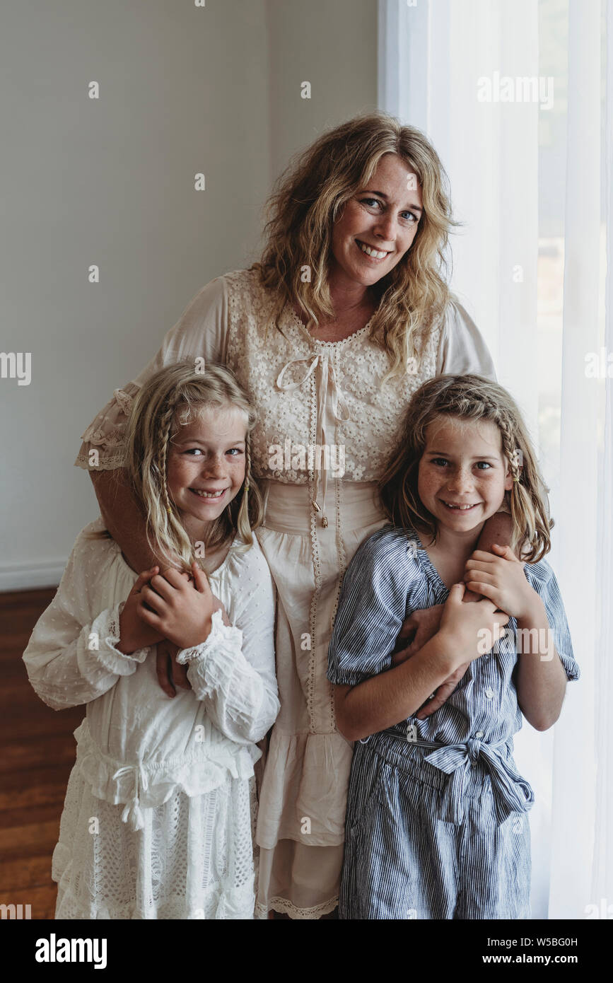Mother and two daughters standing in narual light studio smiling Stock Photo