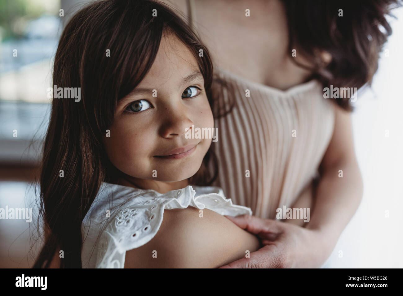 Close up view of school aged girl being hugged by mother Stock Photo