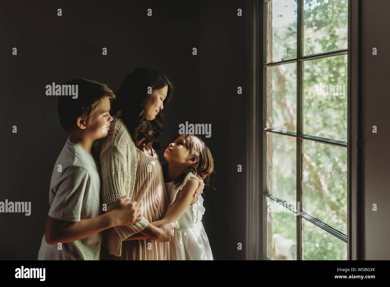 Mother, son, and daughter embrace and look at each other Stock Photo