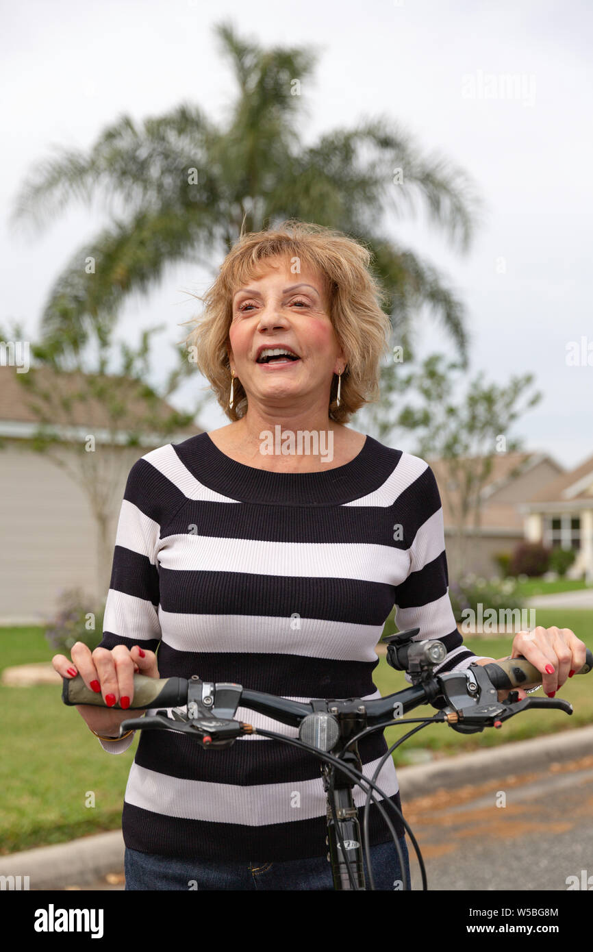 Mature woman in her seventies laughing outside on her bike. Stock Photo