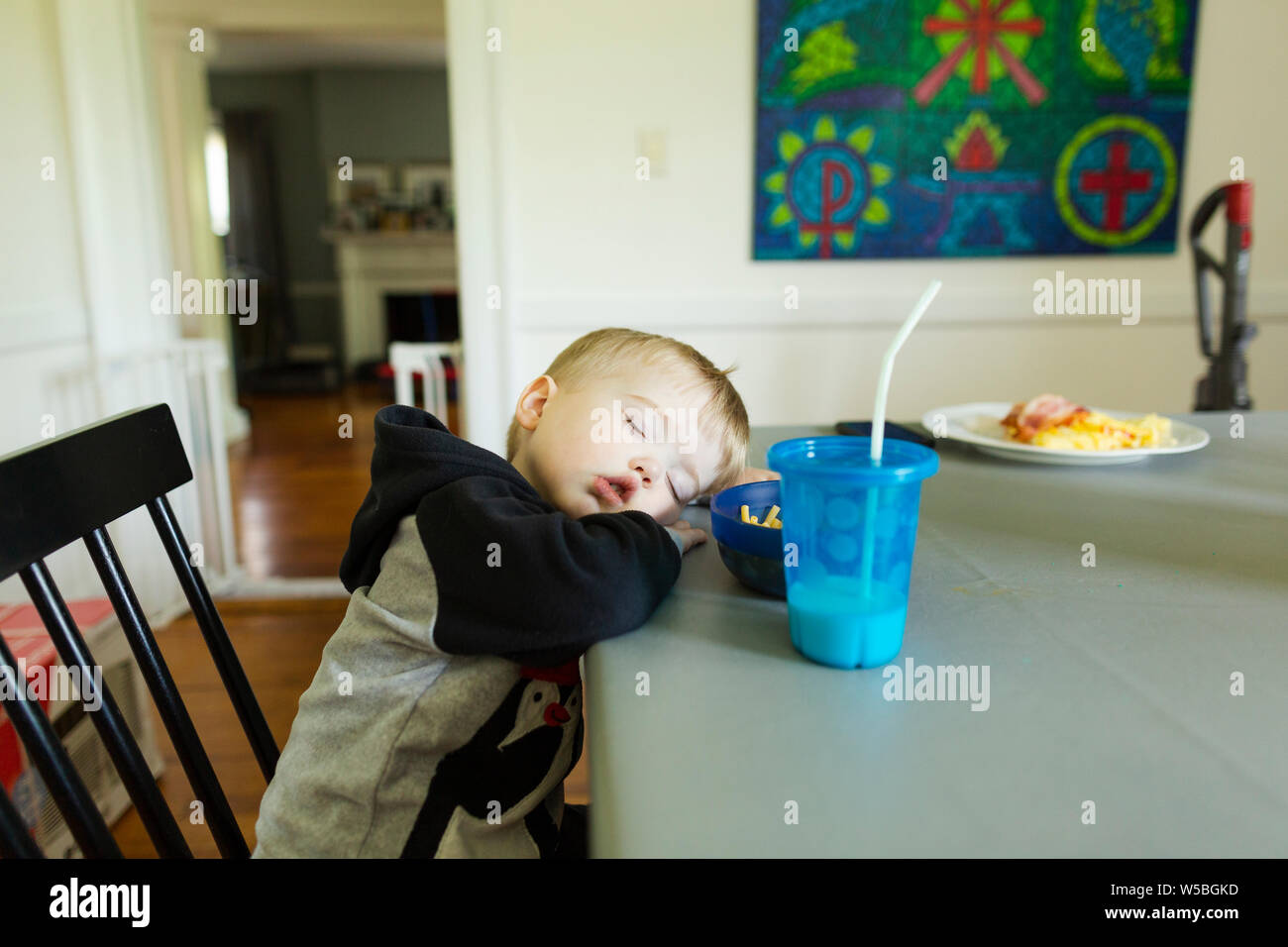 Tired toddler boy falls asleep while sitting in dining room chair Stock