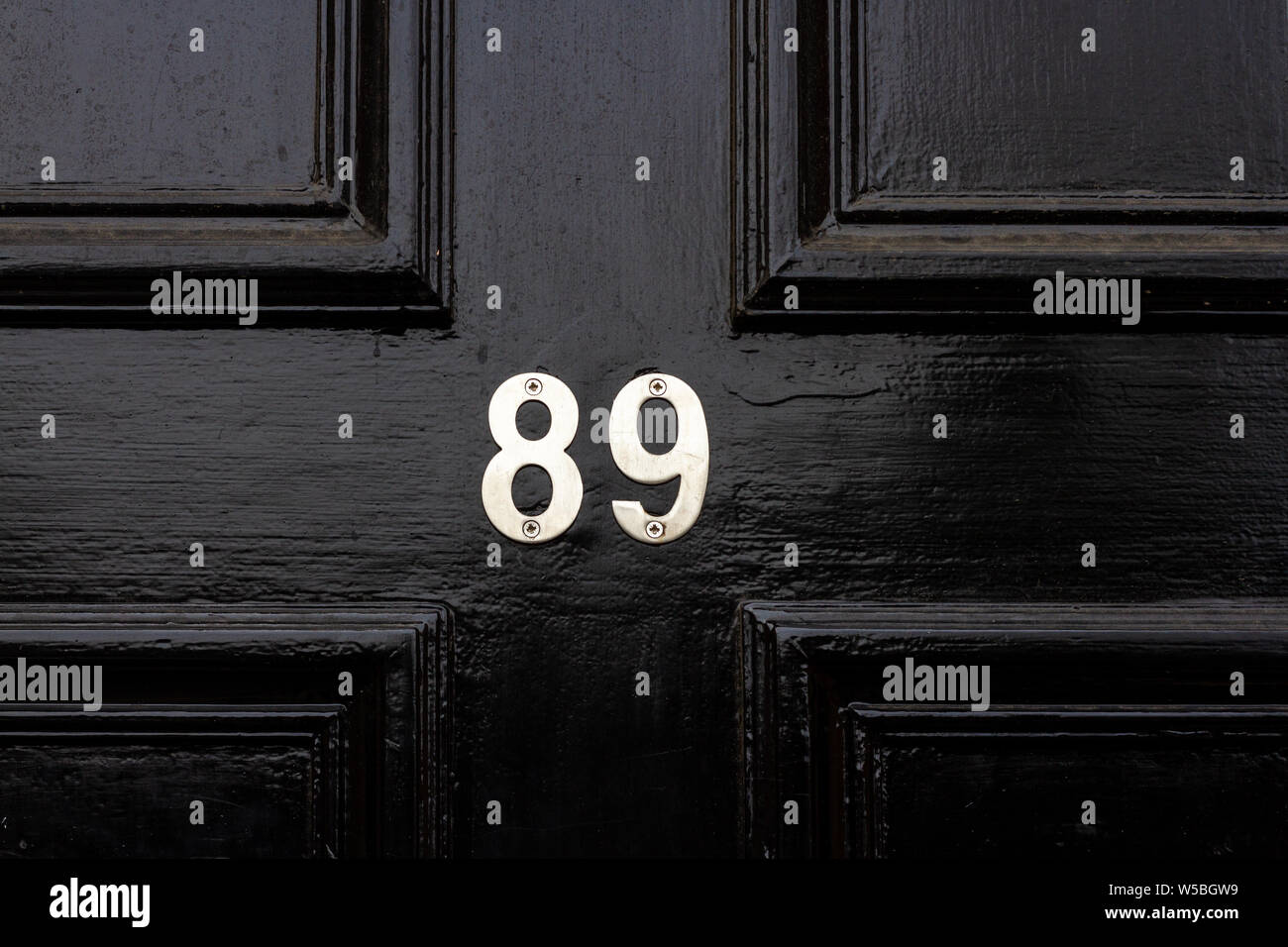House number 89 with the eighty nine in shiny silver numerals on a black wooden front door Stock Photo