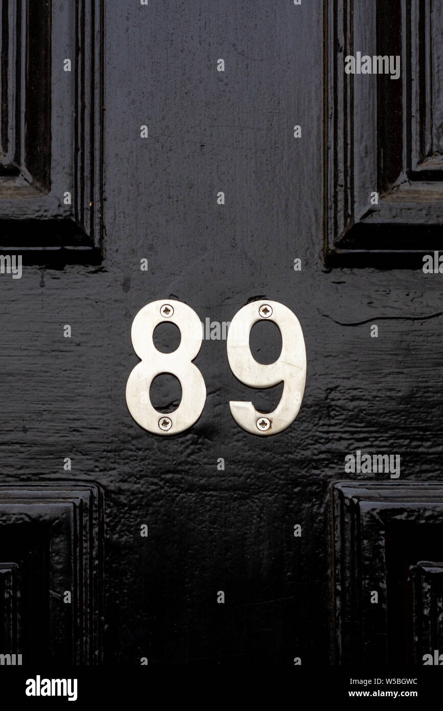 House number 89 with the eighty nine in shiny silver numerals on a black wooden front door Stock Photo