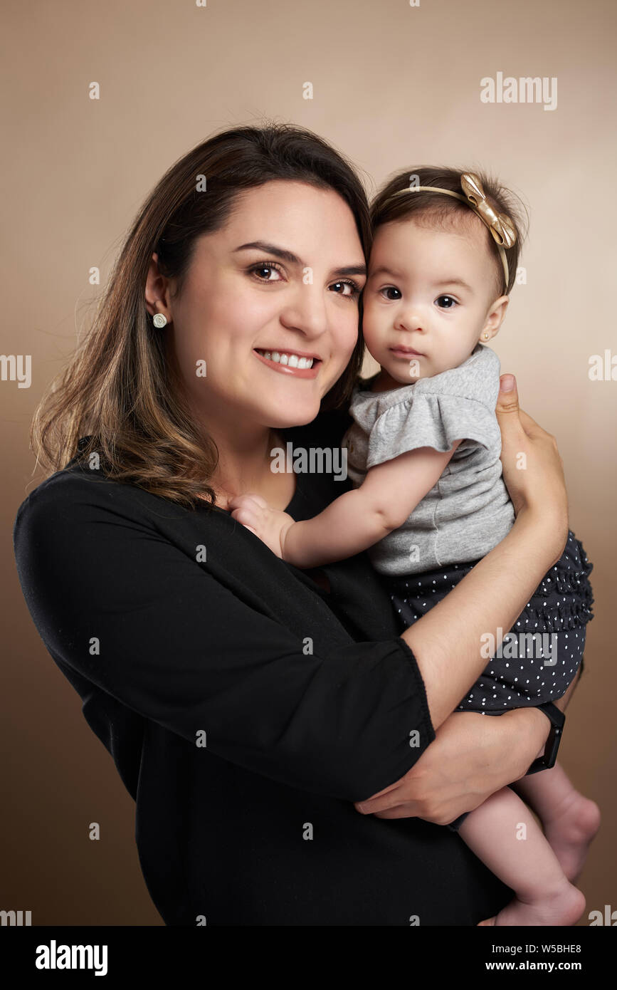 Smiling latin mother holding baby girl in studio background Stock Photo