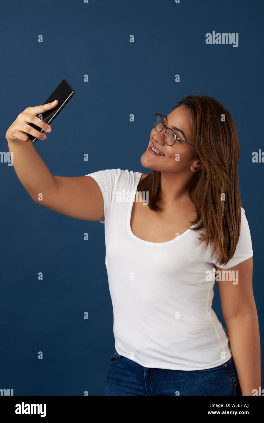 Girl with braces take selfie isolated on blue studio background Stock Photo