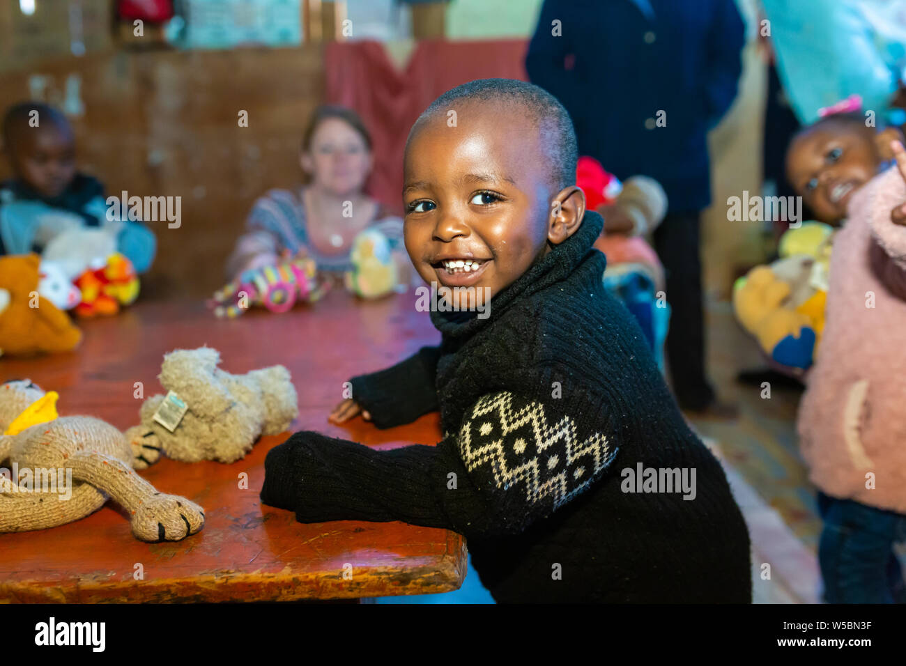Nanyuki, Laikipia county, Kenya – June 10th, 2019: Young smiling Kenyan child sitting at table while at nursery playing with stuffed toys that had bee Stock Photo