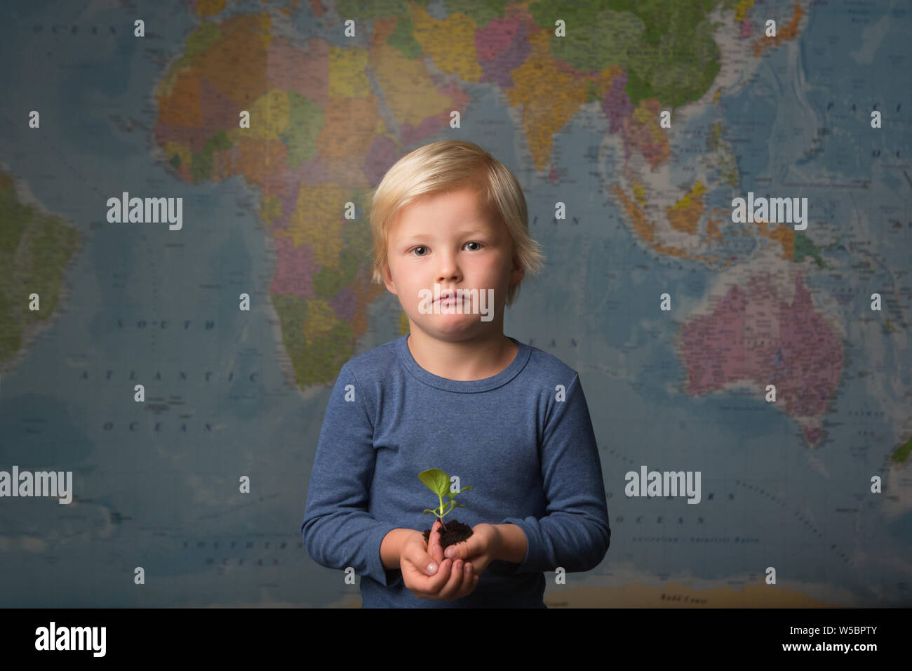 Cute blonde boy holds seedling in front of world map Stock Photo