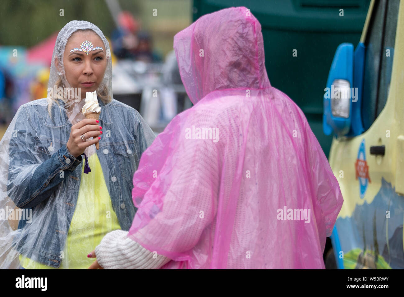 Standon, UK. Saturday 27 July 2019.  festival attendees eating ice cream wearing ponchos in the rain at Standon Calling set in the picturesque grounds of Standon Lordship © Jason Richardson / Alamy Live News Stock Photo