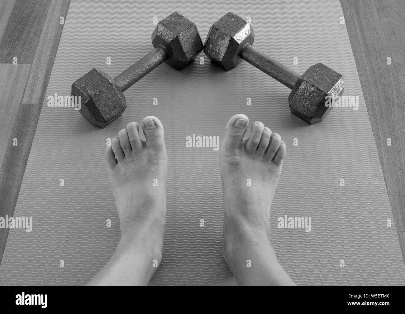 Black and white version of Feet and Dumbbells after a home workout on a yoga mat Stock Photo