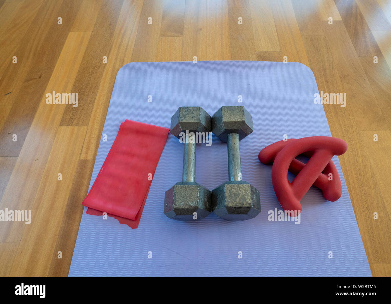 Overhead view of a pair of dumbbells, theraband exercise bands, and a yoga mat on hardwood floor Stock Photo