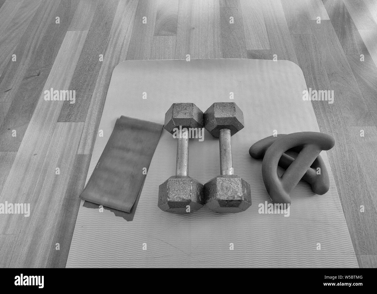 black and white version of Overhead view of a pair of dumbbells, theraband exercise bands, and a yoga mat on hardwood floor Stock Photo