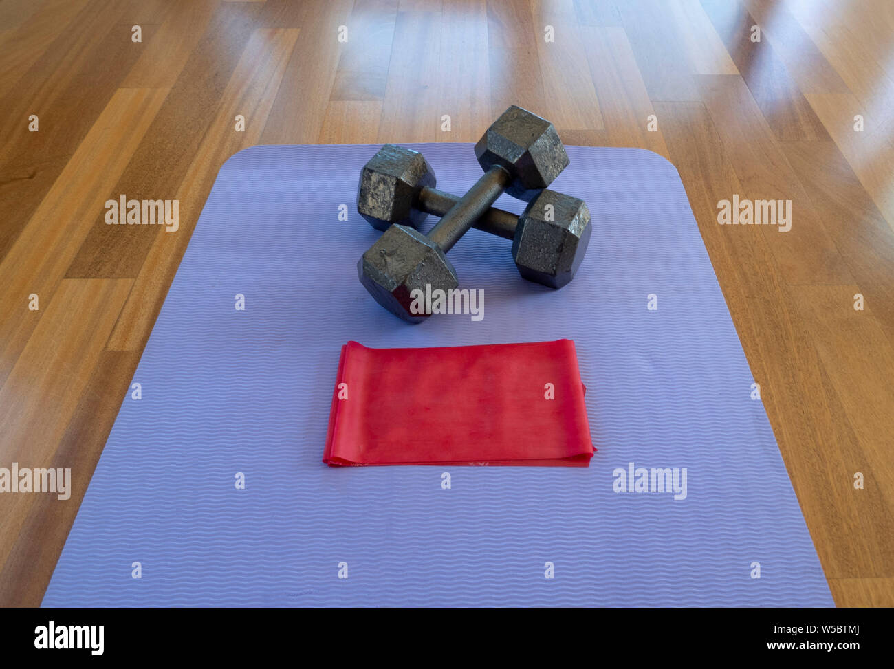 Crossed Dumbbells and Exercise band on a Yoga Mat for a Home workout Stock Photo