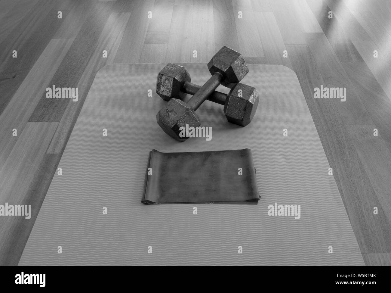 Black and white version of Crossed Dumbbells and Exercise band on a Yoga Mat for a Home workout Stock Photo