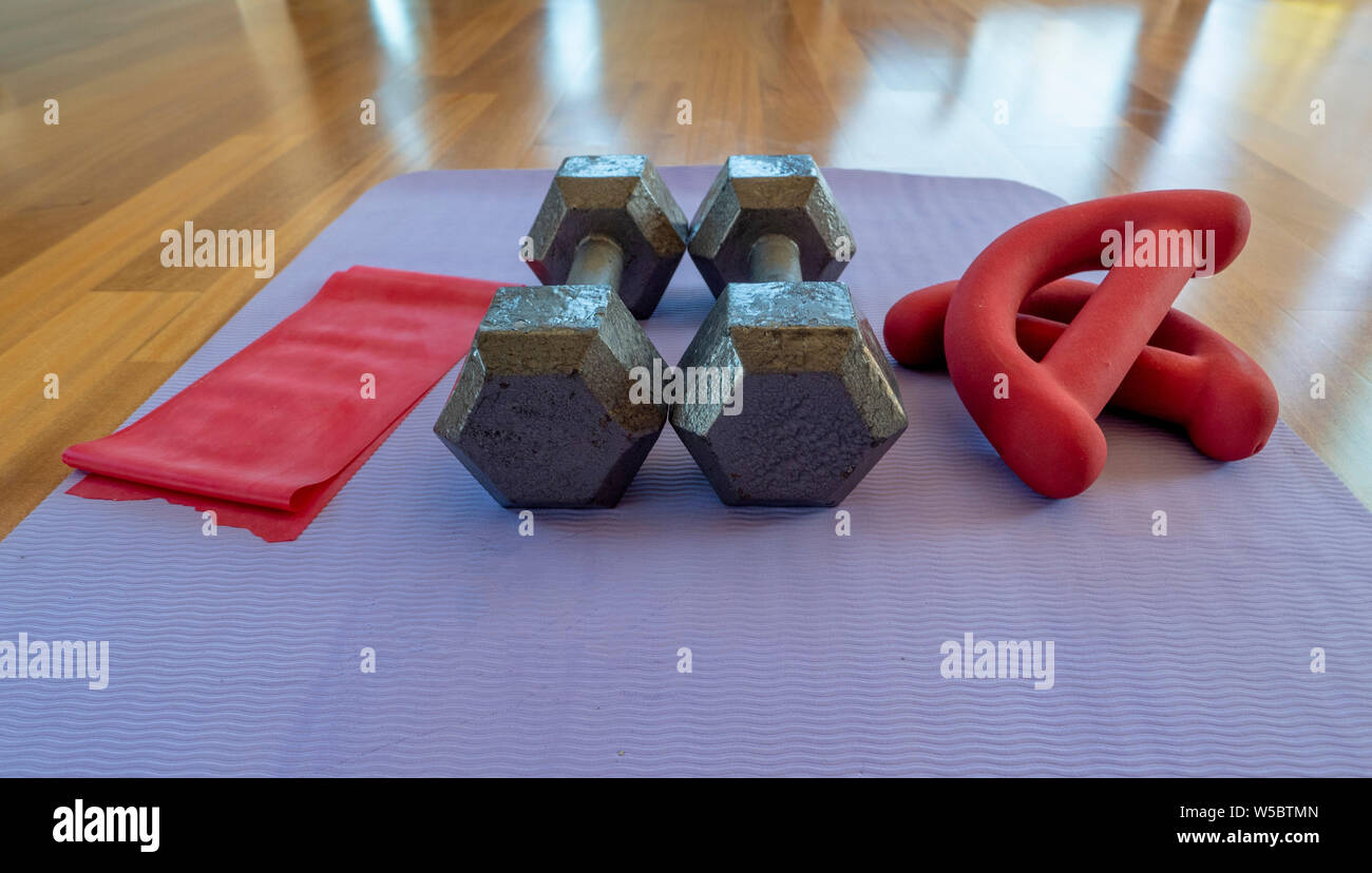 Close up of a pair of dumbbells, theraband exercise bands, and a yoga mat on hardwood floor Stock Photo