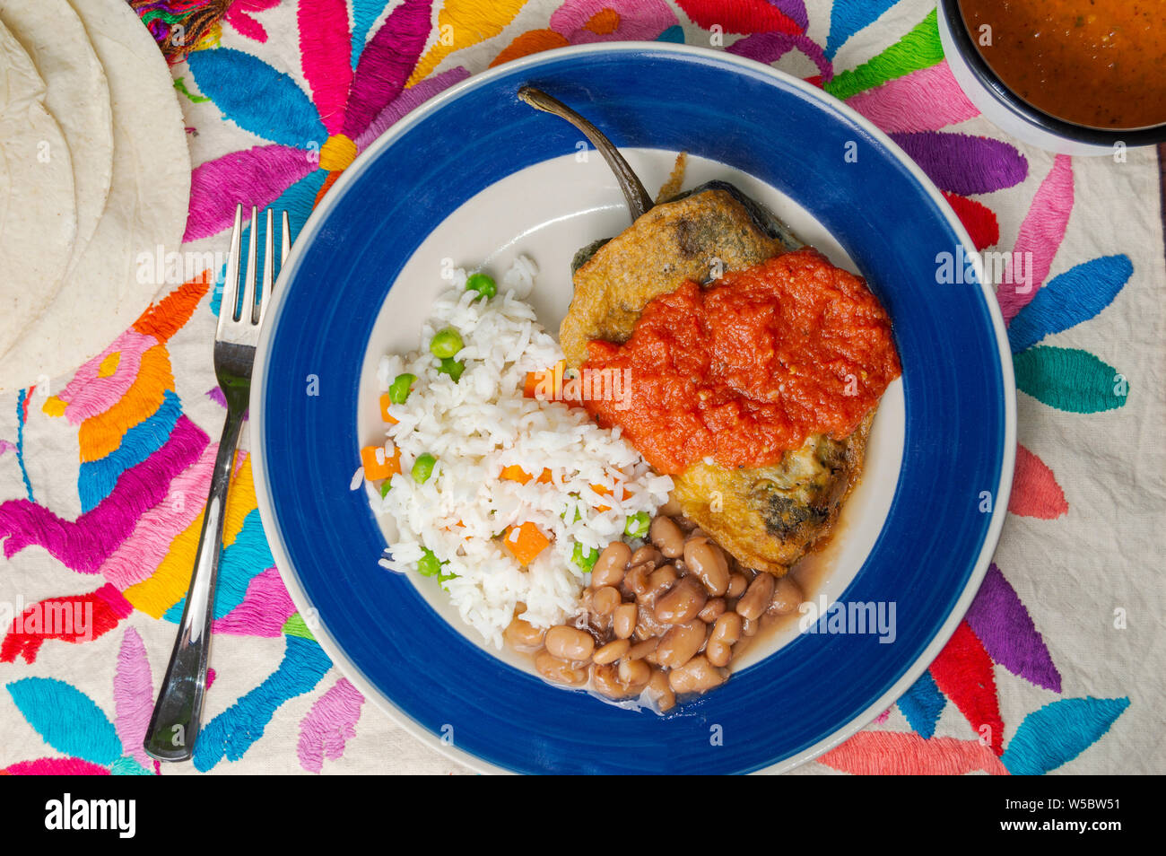 Mexican stuffed chilies (Chiles Rellenos), poblano chilies filled with cheese and coated with a light batter. Served with beans, rice and red tomato s Stock Photo